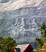 The Carving: the largest high relief sculpture in the world, the Confederate Memorial Carving, depicts three Confederate heroes of the Civil War, President Jefferson Davis and Generals Robert E. Lee and Thomas J. "Stonewall" Jackson. The entire carved surface measures three-acres, larger than a football field. The carving of the three men towers 400 feet above the ground, measures 90 by 190 feet, and is recessed 42 feet into the mountain. The deepest point of the carving is at Lee's elbow, which is 12 feet to the mountain's surface. Stone Mountain is a granite dome located in Stone Mountain, Georgia, a suburb of Atlanta. It is the world's largest exposed mass of granite. At its summit, the elevation is 1,683 feet (513 m) amsl and 825 feet (251.5 m) above the surrounding plateau. It is well-known not only for its geology, but also for the enormous bas-relief on its north face, the largest bas-relief in the world. Three figures of the Confederate States of America are carved there: Stonewall Jackson, Robert E. Lee, and Jefferson Davis. The mountain was the site of the founding of the second Ku Klux Klan in 1915, and the Klan was intimately involved in the design, financing, and early construction of the monument. However, they were not the originators of the idea